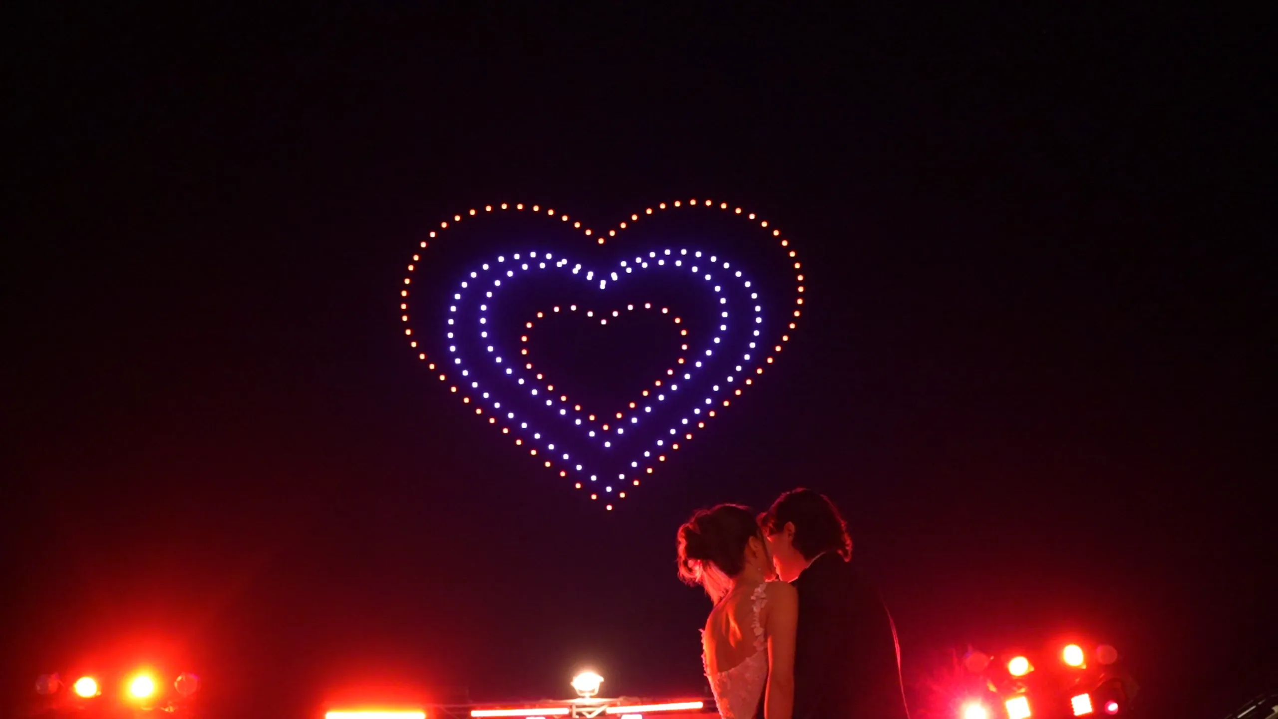 Christina and Andrew beneath three nested hearts formed by drones at Alila Villas Uluwatu, Bali.